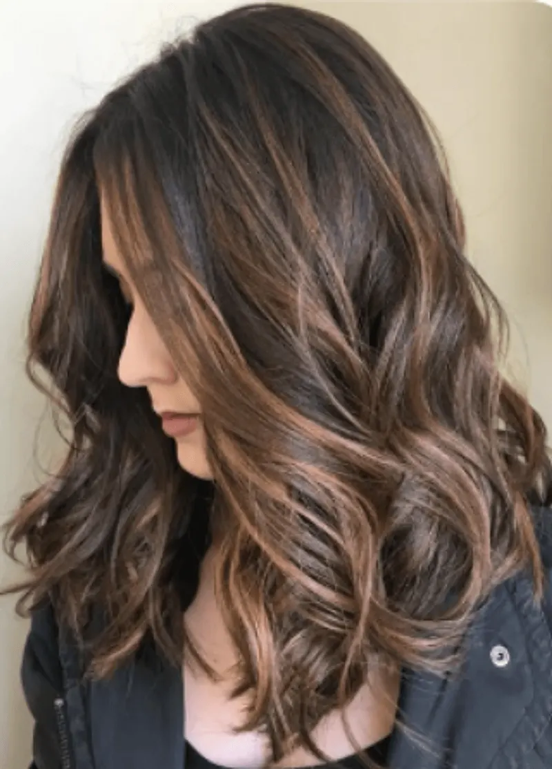 A woman with layered wavy brunette hair and warm caramel highlights